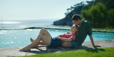 a man and woman sitting next to each other on the ground near a swimming pool