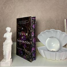 a book sitting on top of a white shelf next to a vase and bowl filled with flowers