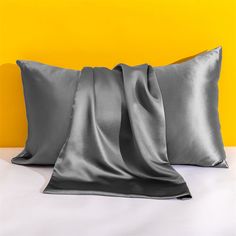 two gray pillows sitting next to each other on top of a white bed with yellow walls