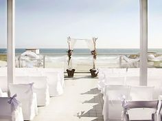 an outdoor wedding set up on the beach with white linen draped over chairs and flower arrangements