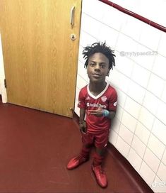 a young man standing in front of a door wearing red soccer shoes and holding a water bottle