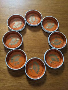 six orange plates arranged in the shape of a circle on a wooden table with leaves painted on them