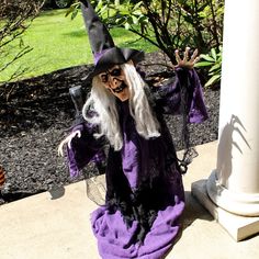 a wizard doll sitting on the ground next to a white column and tree with green leaves