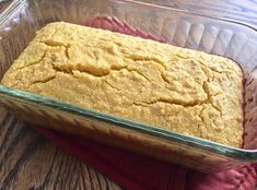 a loaf of bread sitting in a glass dish on top of a red cloth next to a wooden table