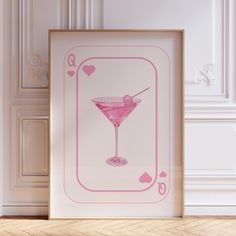 an art print with a pink martini in a frame on the floor next to a white wall