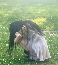 a woman with long black hair kneeling down in the grass