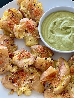 a white plate topped with potato wedges next to a bowl of green dipping sauce