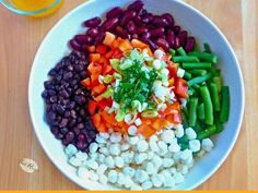 a white bowl filled with beans, carrots and celery next to a glass of orange juice