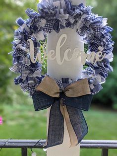 a blue and white wreath with the word welcome hanging on a porch rail next to flowers