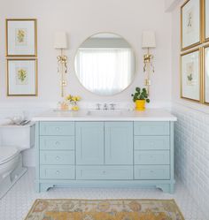 a white and blue bathroom with gold framed pictures on the wall above the vanity area