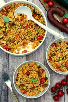 two white bowls filled with rice and vegetables next to a sausage on a wooden table