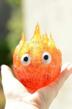 a hand holding up a small orange ball with eyes on it's face and flames coming out of its mouth