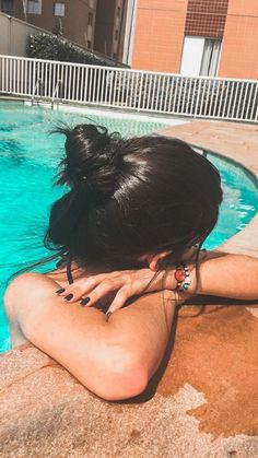 a woman is sitting in the pool with her hands on her head and looking at the water