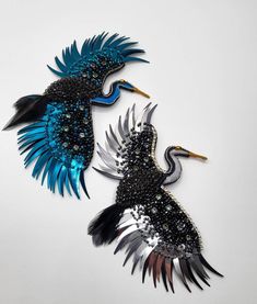 two blue and black birds with long wings on a white surface, one is made out of metal