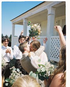 a group of people standing around each other in front of a house with flowers and greenery