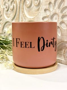 a pink coffee mug with the words feel dirty on it sitting next to some flowers