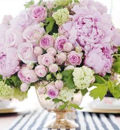 a vase filled with pink and white flowers on top of a striped tablecloth covered table