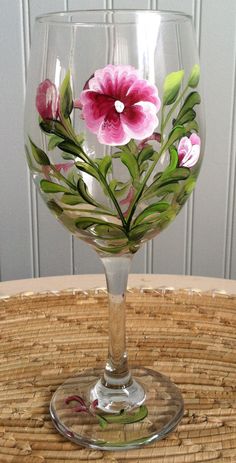 a wine glass with pink flowers painted on the side and green leaves in the middle