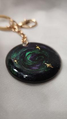 a black and green swirl with gold stars on it's side is hanging from a golden keychain