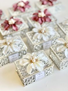 small boxes with flowers on them sitting on a white tableclothed surface, all decorated in silver filigrees