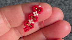 a hand holding a beaded red and white flower in it's left thumb