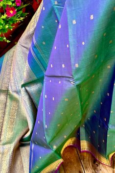 This exquisite kanjivaram silk saree in emerald green shot with ink blue is handwoven with vaira oosi stripes. The boy is adorned with tiny mayil and chakram buttas in gold zari. The traditional borders in geometric and paisley patterns in gold zari, along with a selvedge in magenta pink is nothing but a treat to the eyes. The grand pallu in the same mimics the borders featuring traditional motifs in gold zari. Approximate Length 6.5 mtrs (inclusive of blouse length) Approximate Height - 48 - 52" Approximate weight - 1.7 lbs Saree comes with fall, picot and tassels done when applicable. Blouse piece is cut. Kindly Note : The colors you see on your device may vary due to the color reproduction, brightness and resolution of individual devices. If you'd like more clarity before your purchase, Vaira Oosi Silk Saree, Green Shot, Kanjivaram Silk Saree, Traditional Motifs, Silk Cotton Sarees, Ink Blue, Magenta Pink, Cotton Sarees, Pure Silk Sarees