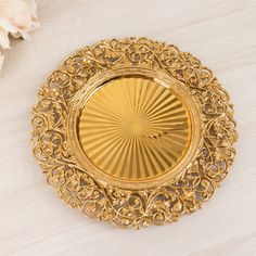 a gold plate with intricate designs on it and white flowers in the backgroud