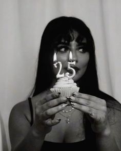 a woman holding up a cupcake with candles in her mouth and the number 25 on it