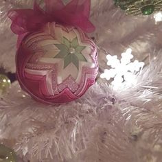 a pink ornament sitting on top of a white christmas tree