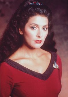 a woman with long hair wearing a red dress and a star trek pin on her shoulder