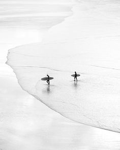 two surfers are walking along the beach with their surfboards