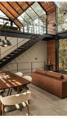 a living room filled with furniture next to a wooden table and stair case in front of a glass wall