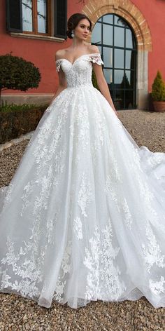 a woman standing in front of a building wearing a wedding dress with white flowers on it