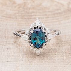 a ring with a blue stone surrounded by white and black diamonds on a wooden surface