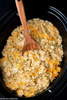 a wooden spoon in a slow cooker filled with rice and cheese, ready to be cooked