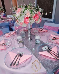 the table is set with pink napkins, silverware and flowers in vases