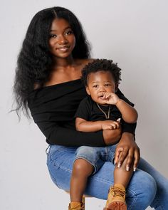 a woman holding a small child in her lap and smiling at the camera while sitting on a stool