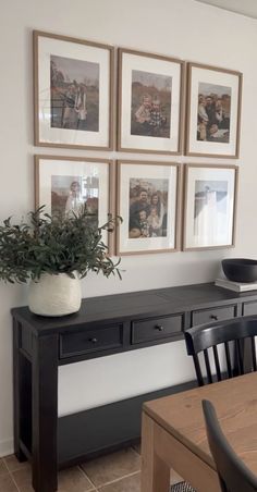 a dining room table and chairs with pictures on the wall above it, along with a potted plant