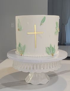 a white cake with green leaves and a gold cross on top is sitting on a table