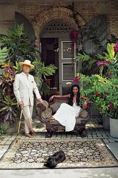 a man in a white suit and hat standing next to a woman sitting on a couch