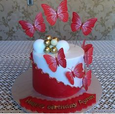 a red and white birthday cake with butterflies on it's top is decorated with gold balls