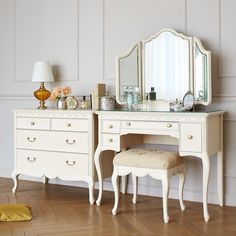 a white dressing table with a mirror and stool next to it on a hard wood floor