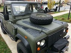 an army green jeep parked on the side of a road next to a sidewalk and grass area