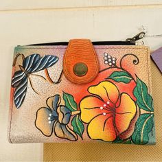 a purse with flowers painted on it and a butterfly hanging from the front, next to a card holder