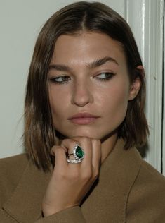 a woman wearing a green ring and brown coat