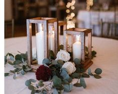 two candles are sitting on a table with flowers and greenery