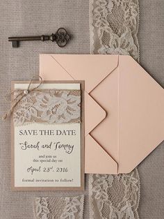 the wedding stationery is laid out next to an envelope and key on top of lace