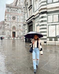 a woman walking in the rain with an umbrella over her head and wearing ripped jeans