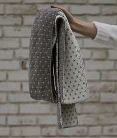 a person holding up a piece of cloth in front of a brick wall with white dots on it