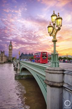 a red double decker bus driving over a bridge at sunset with the big ben clock tower in the background